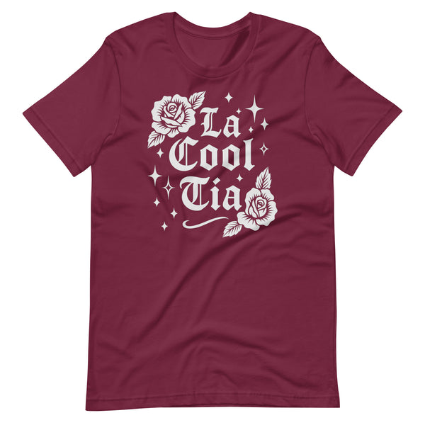 Maroon T-shirt with white gothic-style text that reads “La Cool Tía,” decorated with two rose illustrations and small sparkling star accents around the design.