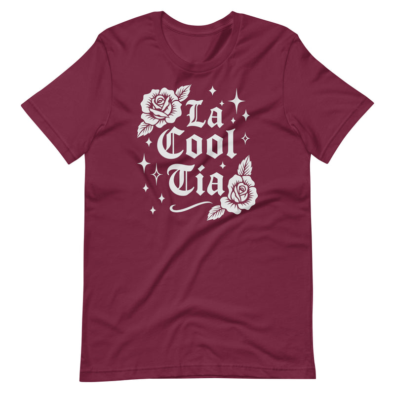 Maroon T-shirt with white gothic-style text that reads “La Cool Tía,” decorated with two rose illustrations and small sparkling star accents around the design.