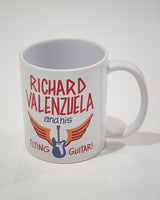 White ceramic mug with vintage-style text that reads 'Richard Valenzuela and his Flying Guitar' with an image of a blue guitar and orange wings from Sew Bonita in Corpus Christi, Texas