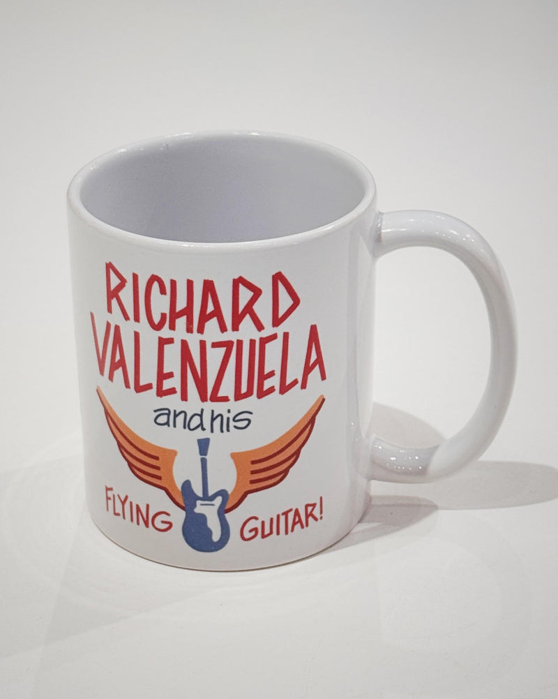 White ceramic mug with vintage-style text that reads 'Richard Valenzuela and his Flying Guitar' with an image of a blue guitar and orange wings from Sew Bonita in Corpus Christi, Texas