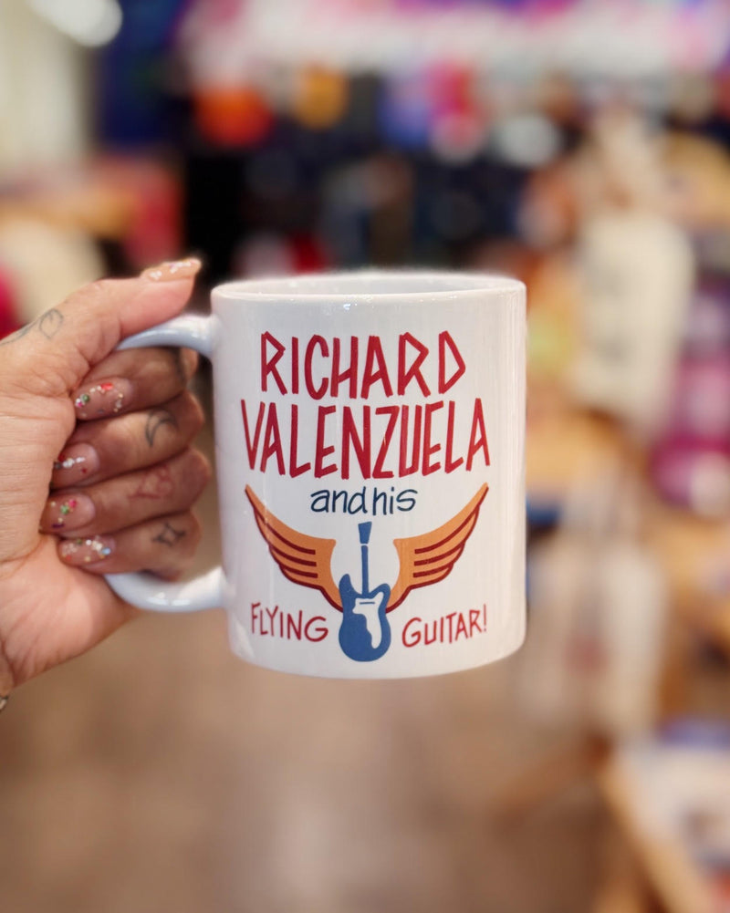 White ceramic mug with vintage-style text that reads 'Richard Valenzuela and his Flying Guitar' with an image of a blue guitar and orange wings from Sew Bonita in Corpus Christi, Texas