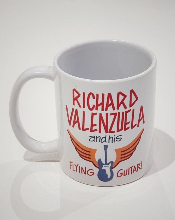 White ceramic mug with vintage-style text that reads 'Richard Valenzuela and his Flying Guitar' with an image of a blue guitar and orange wings from Sew Bonita in Corpus Christi, Texas